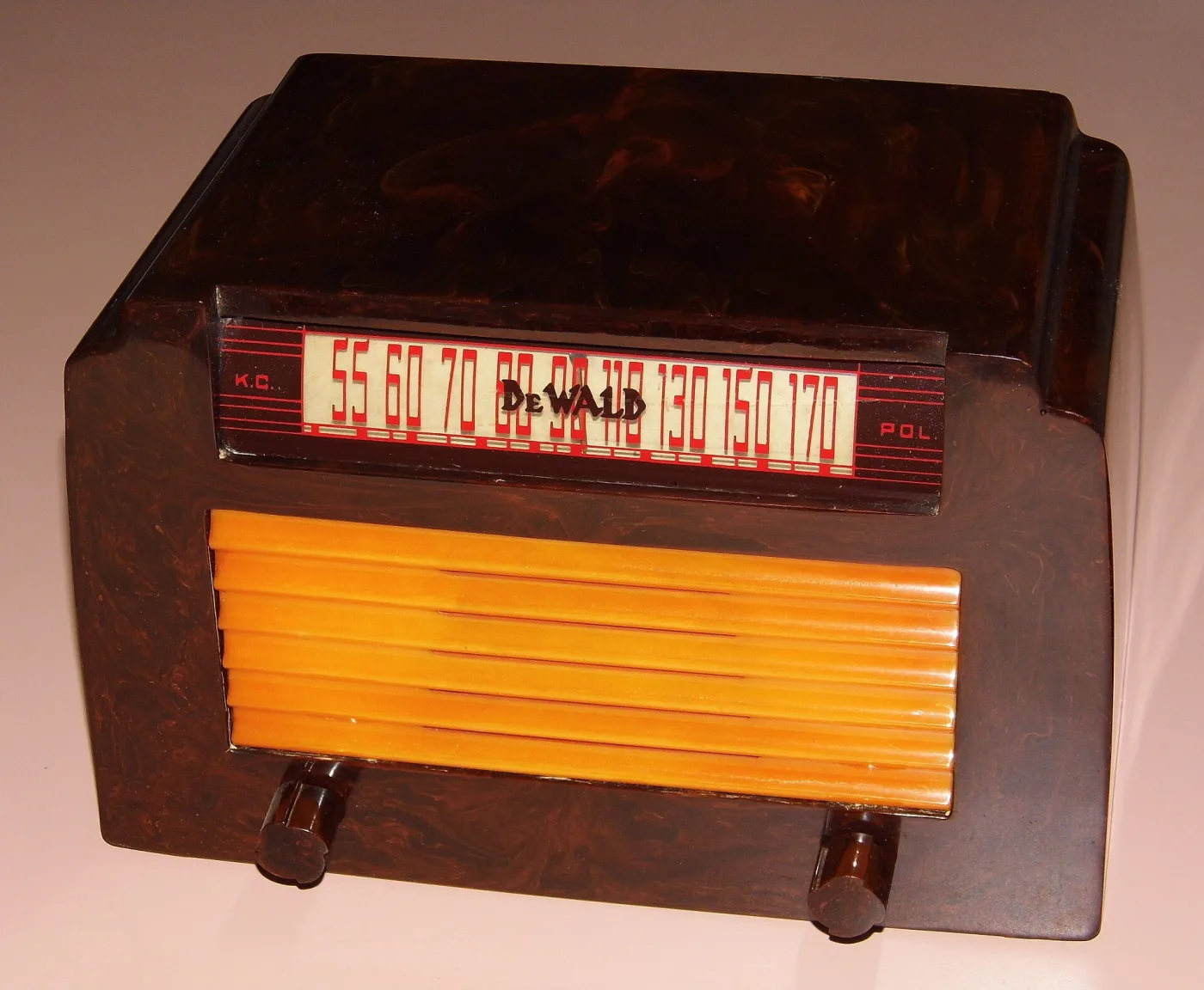 Table radio of about 1946 in dark red-brown swirled cast plastic with a butterscotch-yellow horizontal grille, standing on a patterned surface