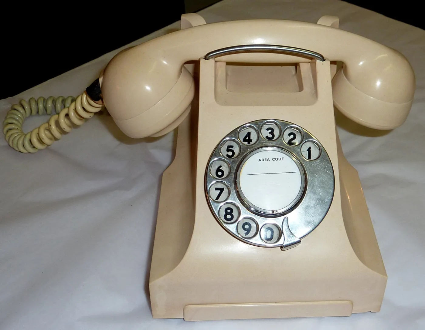 Ivory-coloured Bakelite desk telephone with a curved handset resting on a cradle above a circular finger dial, and a fabric-covered cord