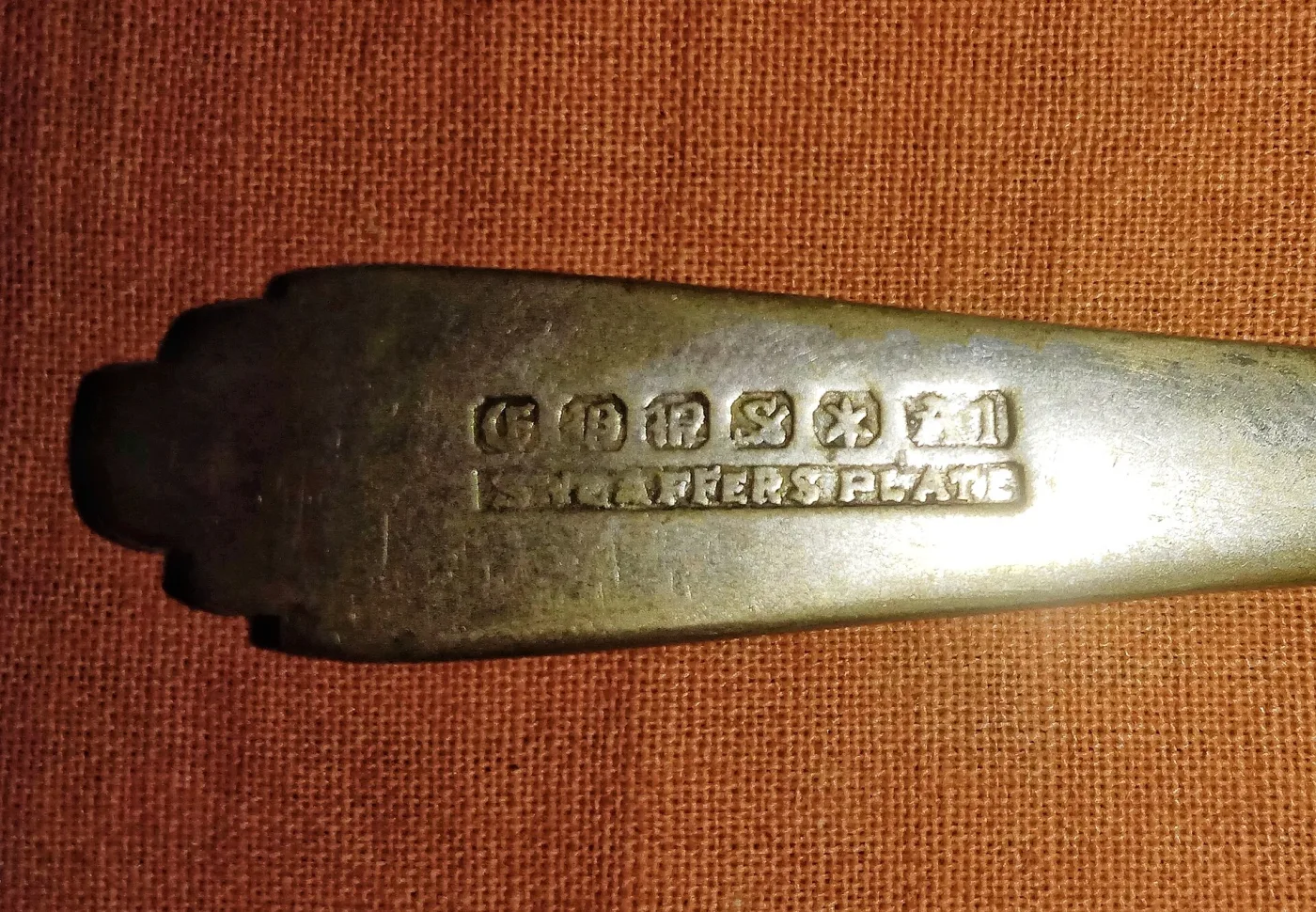 Spoon handle struck with a row of pseudo-hallmark punches above a rectangular stamp reading SHEAFFERS PLATE