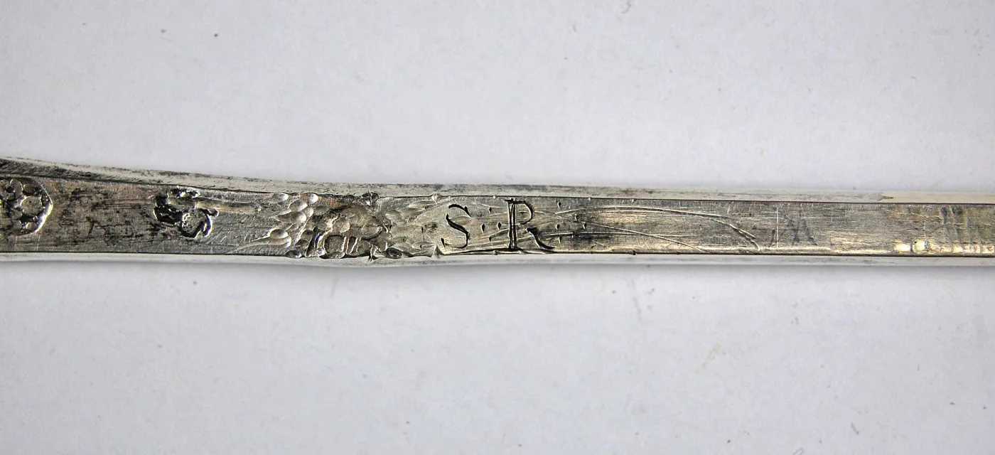 Silver spoon stem showing struck hallmark punches on the left and finely engraved owner's initials S R on the right