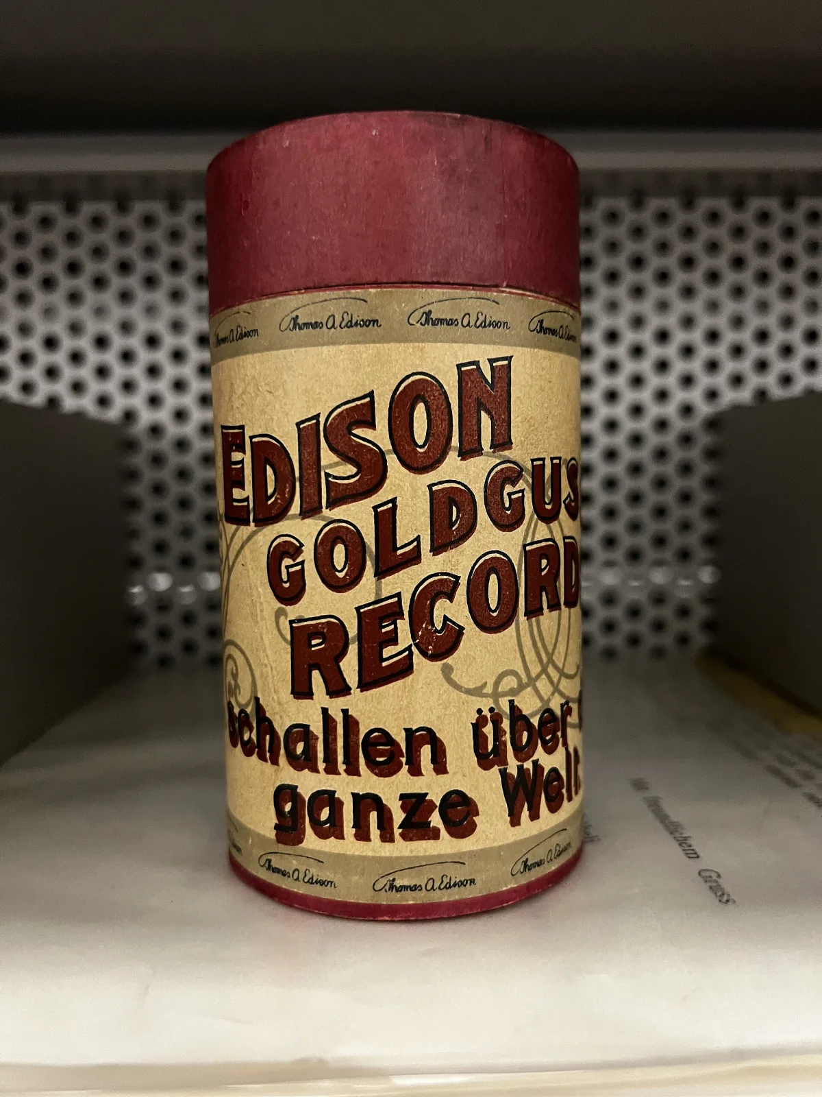 Cardboard cylinder record tube standing on a shelf, printed in red and yellow with the words Edison Gold Moulded Record and German lettering around it