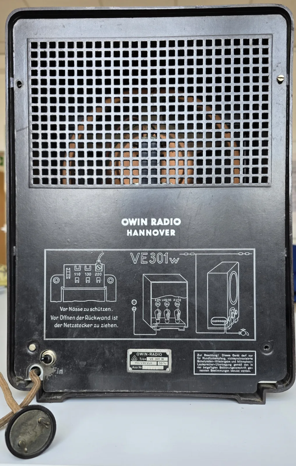 Rear of a 1930s radio with the back panel removed, showing a perforated metal screen, a printed circuit diagram label, terminal screws and the valve chassis behind