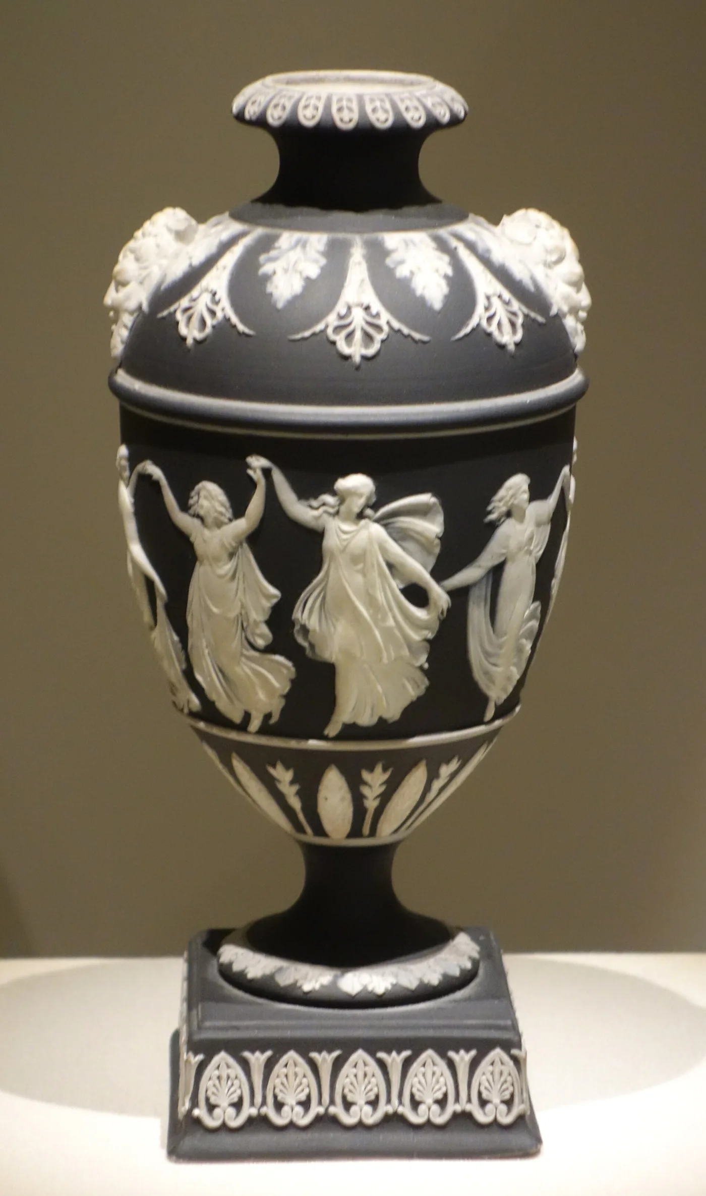 Black Wedgwood urn on a square plinth with applied white classical dancing figures around the body